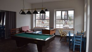 A pool table with four lights above it, a window with a view of a balcony, and a seating area with a table and chairs. - Hotel Ostende (Chocerady)