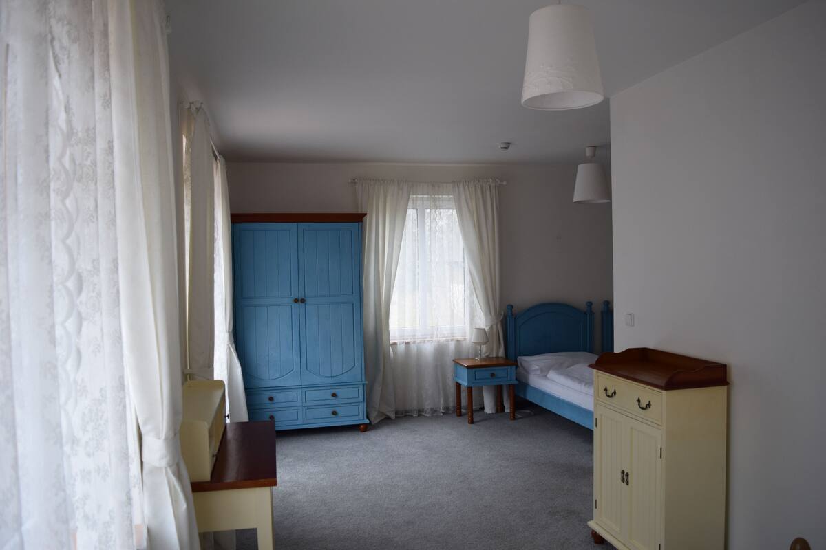 A bedroom with a bed, a blue wardrobe, a small table, and a nightstand.