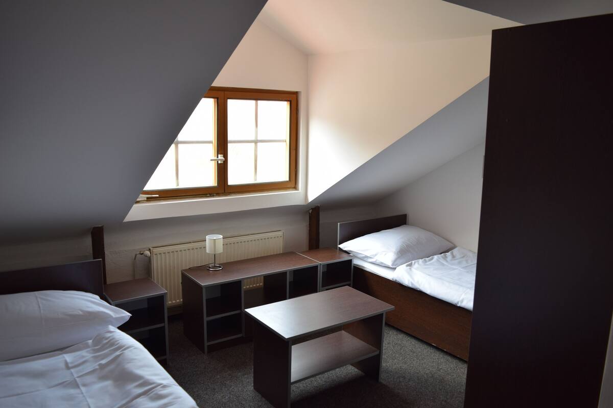 A small, triangular room with a single bed, a desk, and a window.