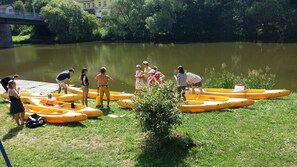 A group of people preparing for a water activity near a river, with several yellow inflatable boats and a bridge in the background. - Hotel Ostende (Chocerady)