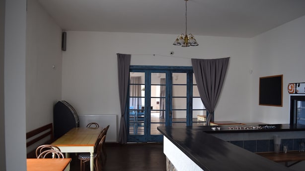 A kitchen with a wooden table and chairs, a black countertop, and a view through a blue-framed door. - Hotel Ostende (Chocerady)