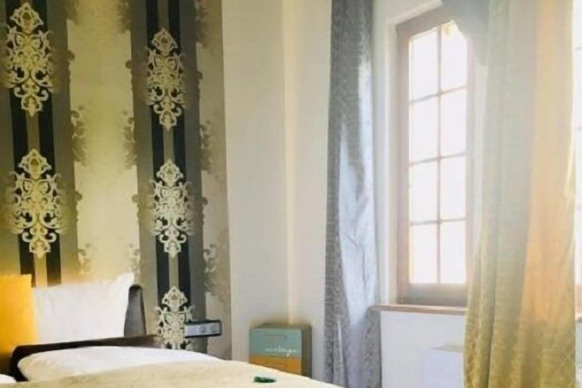 A bedroom with a bed, a bench, curtains, and a window.
