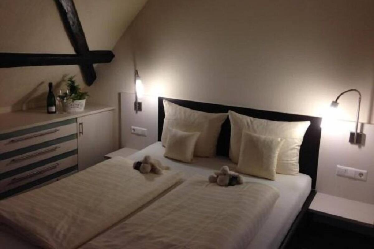 A bedroom with a bed, bedside lamps, a dresser, and a small plant on the dresser.