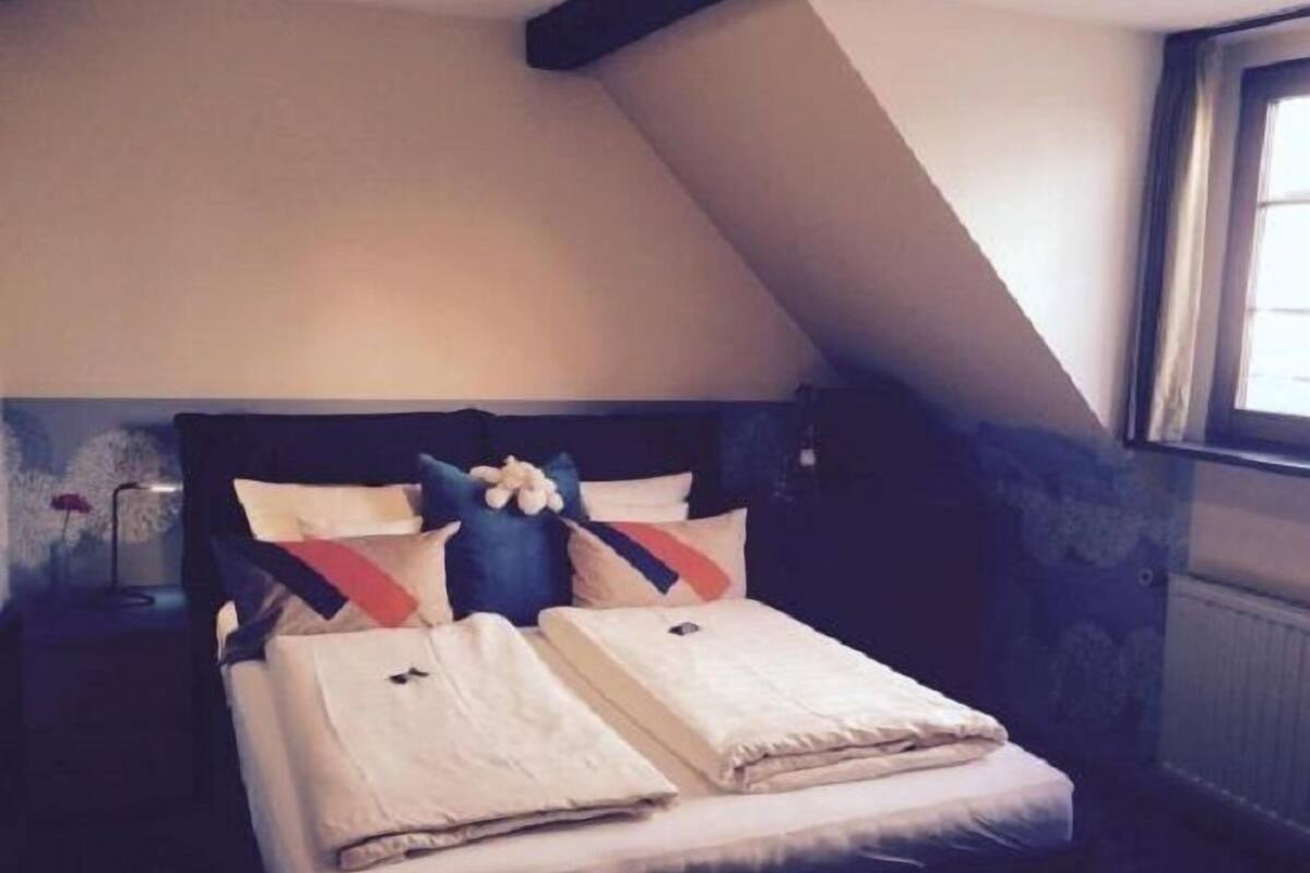A bedroom with a bed, pillows, a nightstand, and a window.