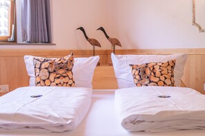 Ett hotellrum med två sängar, båda med vita sängkläder och kuddar med ett träliknande mönster. På väggen hänger två skulpturer föreställande fåglar, tillverkade av trä.