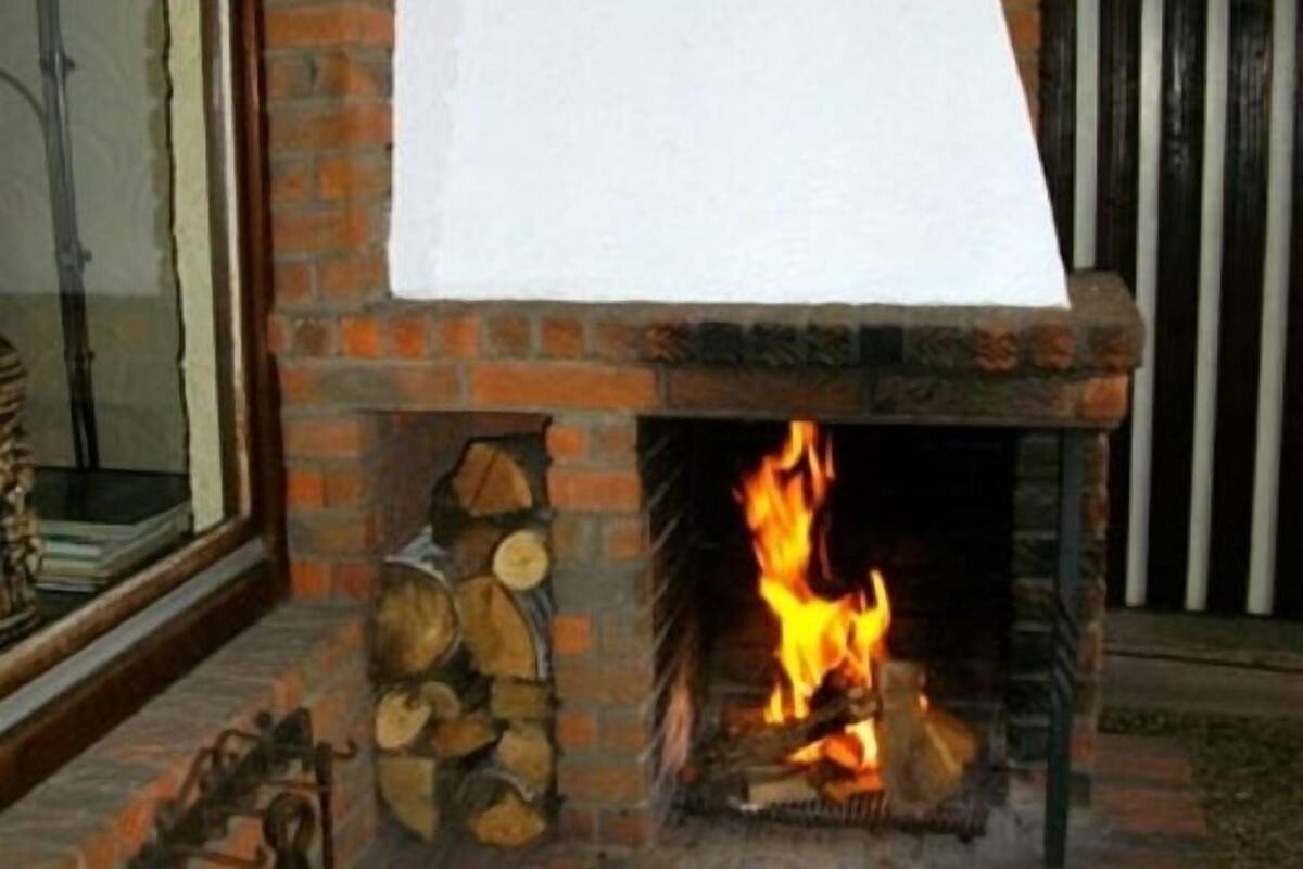 A brick fireplace with a white fire screen, logs stacked beside it, and a metal fireguard.