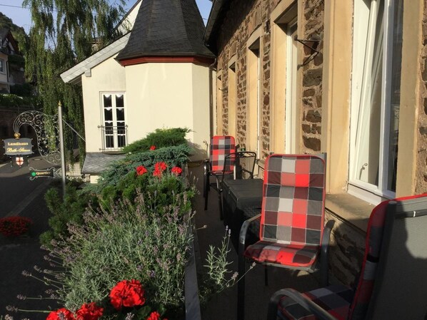 En pittoresk byggnad med en fasad av sten, en liten trädgård med röda blommor och utomhusmöbler med rutiga stolar.