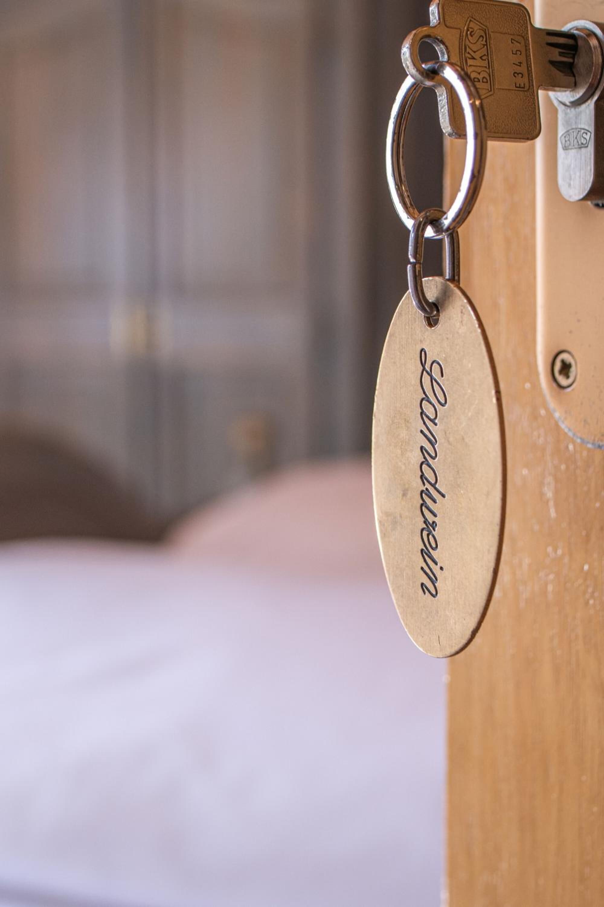 Ein Schlüsselanhänger mit der Aufschrift 'Landhaus', befestigt an einem Metallring, vermutlich für ein Hotelzimmer.