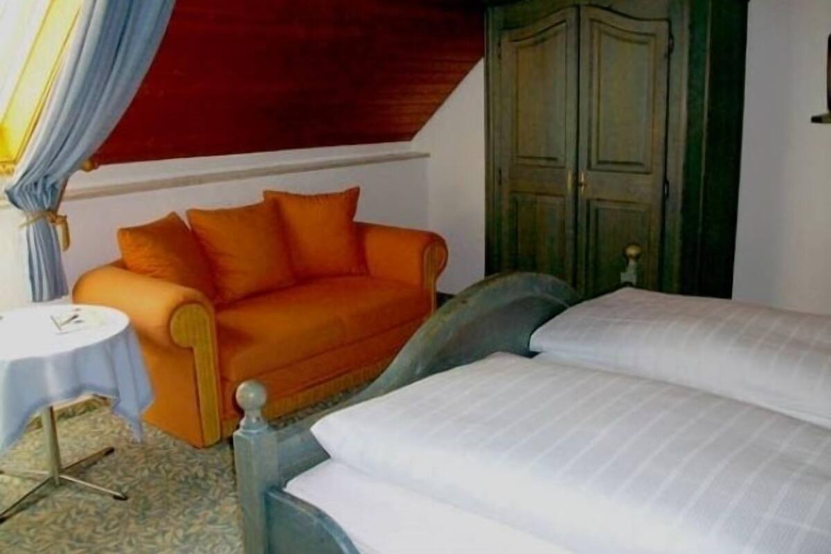 A room with a bed, an orange sofa, a green wardrobe, and a small round table.