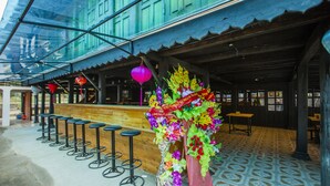 A bar area with a long counter, multiple stools, and a decorative floral arrangement. - Ngoc Son homestay (Ha Giang 1)