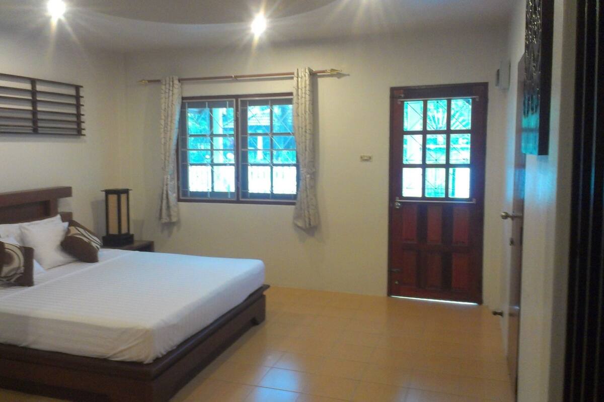 Un dormitorio con cama, ventana, puerta y mesita de noche.