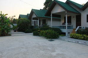 A row of single-story houses with green roofs and white walls, each with a porch and a small garden area.