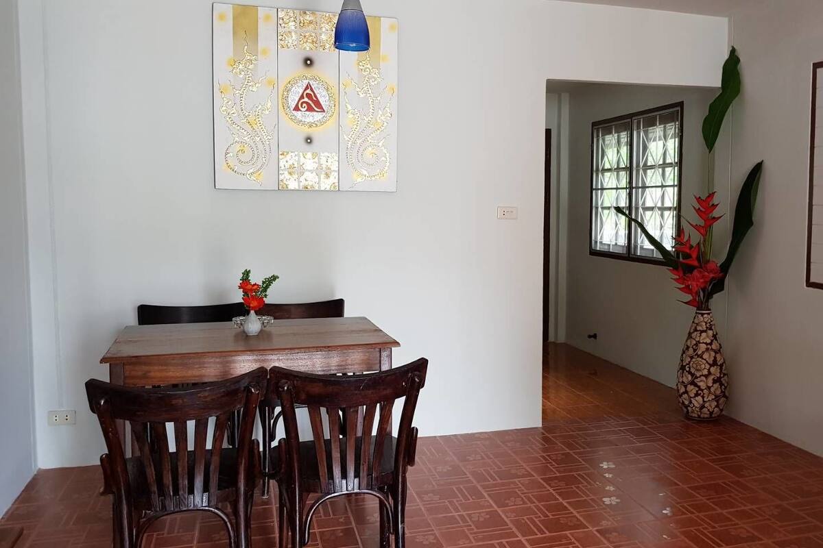 Un comedor con una mesa y sillas de madera, un adorno en la pared y una planta grande.