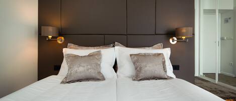 A double bed with two pillows, a headboard with a light fixture, and a glass door leading to a bathroom.