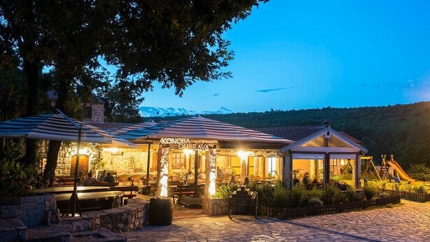 Um restaurante com mesas ao ar livre, paredes de pedra e vista para a paisagem circundante.