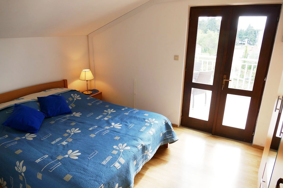 Un dormitorio con una cama, una mesita de noche, una lámpara y una puerta que da a un balcón.