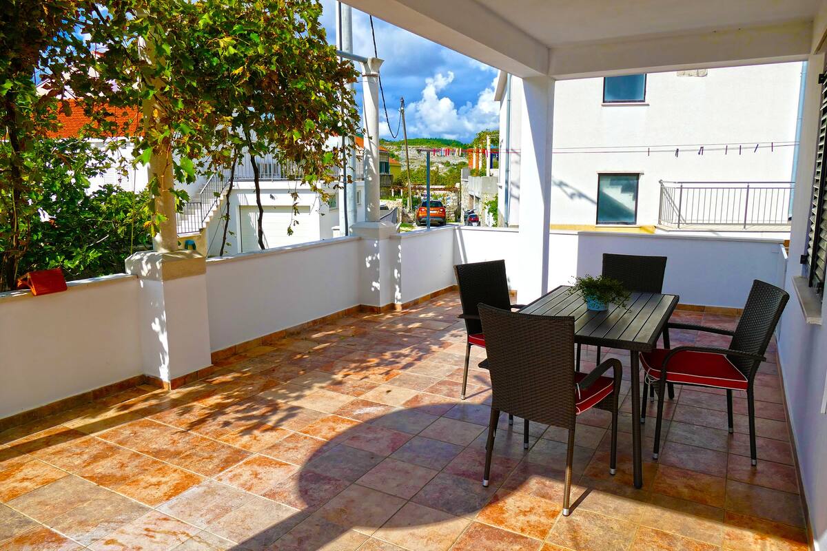Un patio al aire libre con una mesa y sillas, una planta en maceta y vistas de un edificio con balcones.