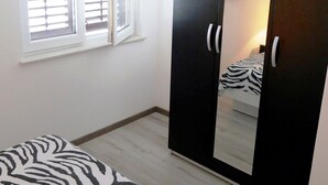 Quarto com cama, guarda-roupa com espelho e janela com persianas.