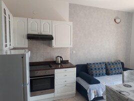A compact kitchen with white cabinets, a built-in oven, and a kettle on the counter.