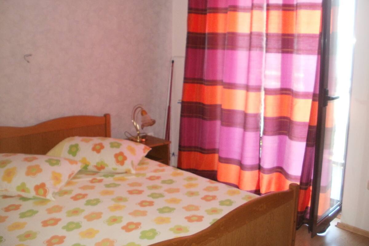 A bedroom with a bed, a nightstand, and a window with curtains.