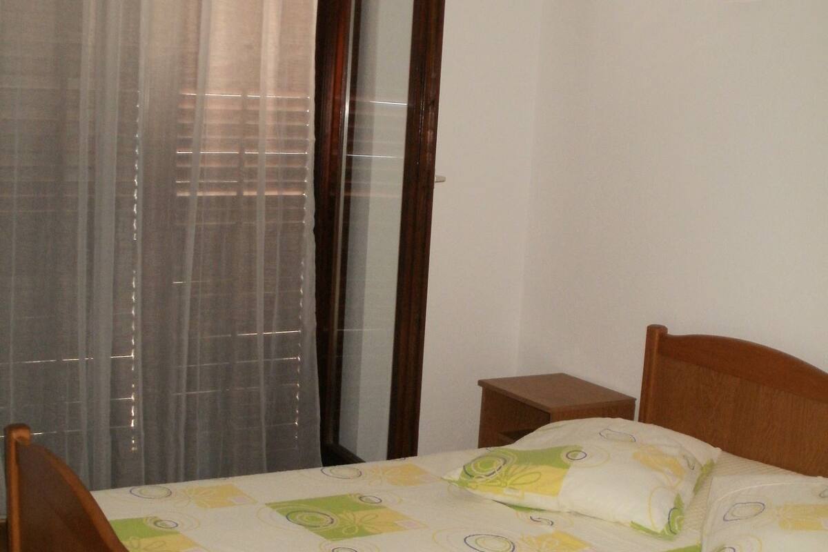 A bedroom with a wooden bed, a bedside table, and a window with sheer curtains.