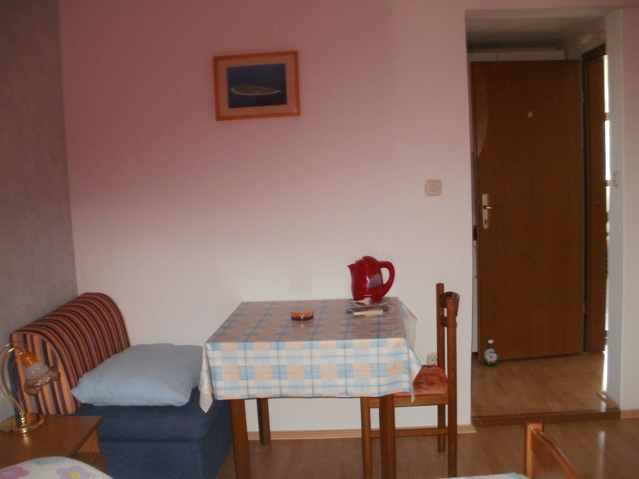A small room with a checkered table, a red pitcher, a blue sofa, and a wooden door.