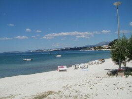 A beach with white sand, a row of white lounge chairs, and a few boats in the water.