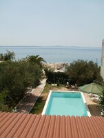A swimming pool with a view of the sea, surrounded by greenery and a stone pathway.