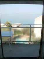 A balcony with a view of the sea, a small table, and a metal railing.