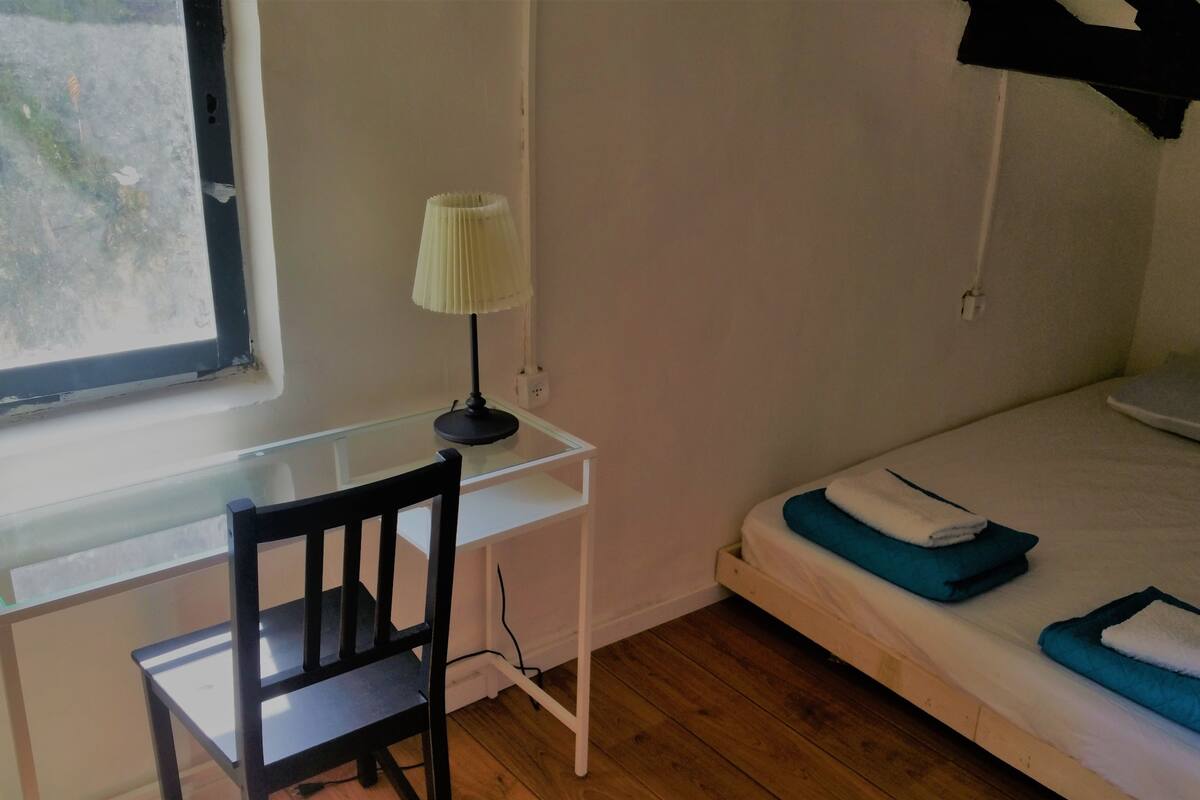 Ein Schlafzimmer mit einem Einzelbett, einem Schreibtisch mit Stuhl und einem Fenster.