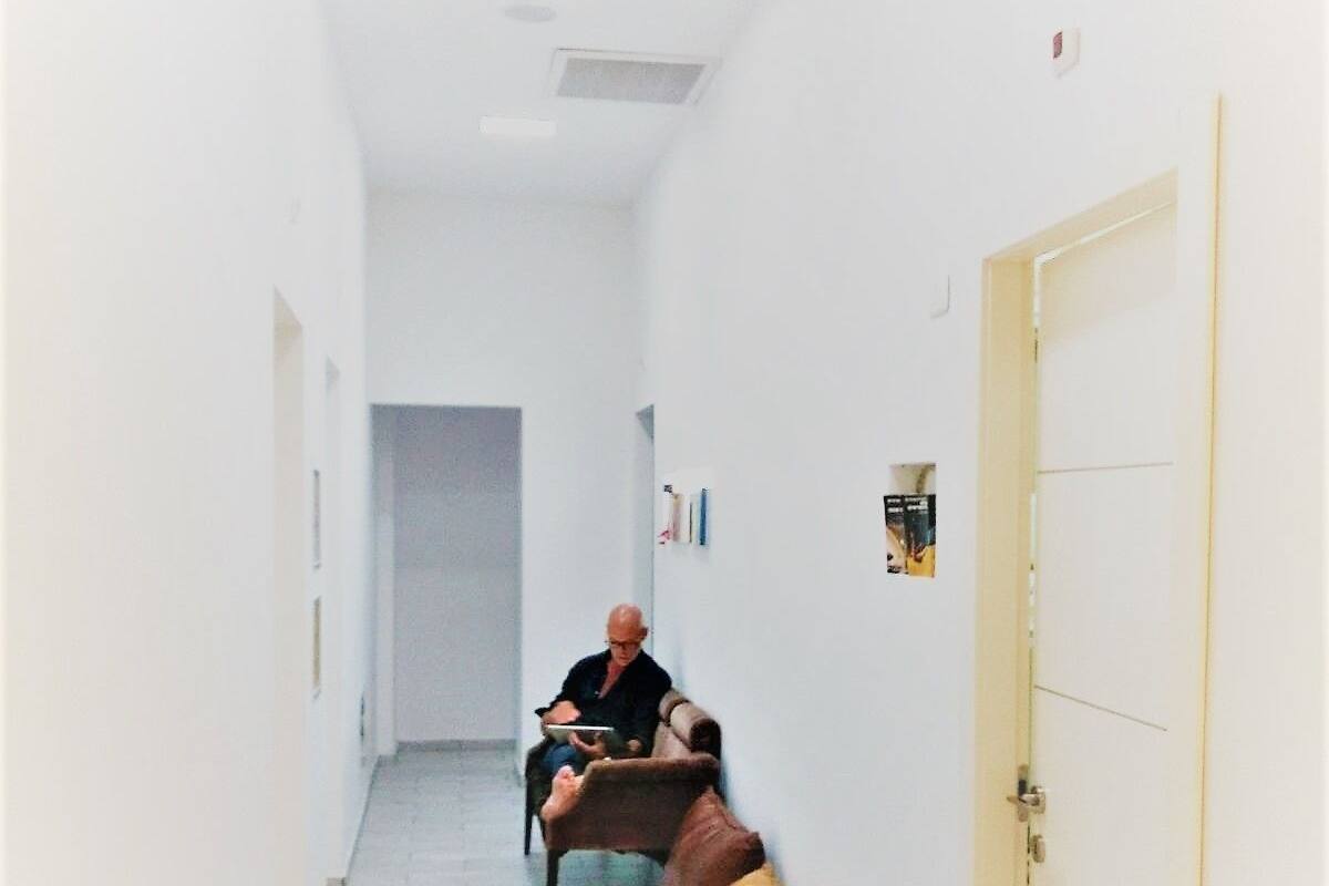 Ein schmaler Flur mit einer braunen Couch, einer Tür rechts und einem hellen Boden.