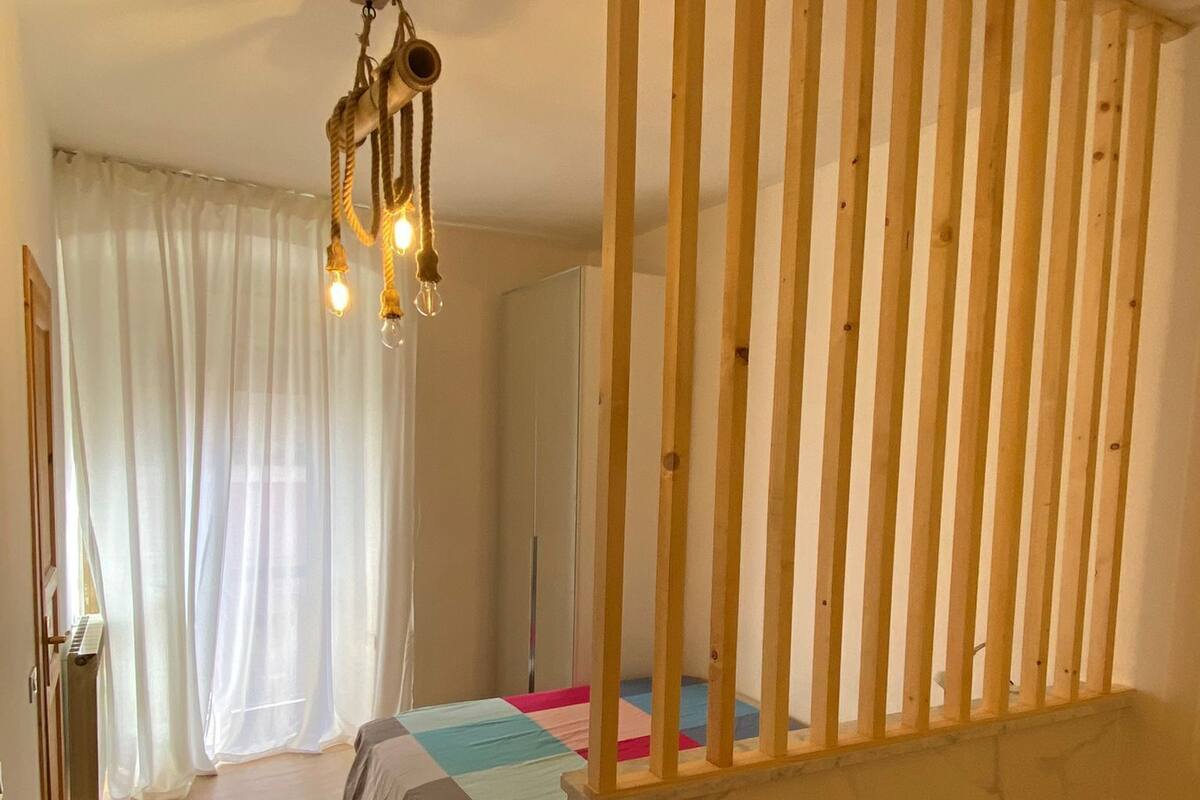 Quarto com cama, divisória de madeira, luminária pendente e radiador.