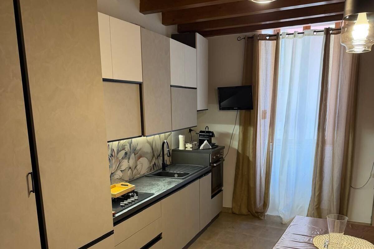 Cozinha com pia, fogão e armários, uma mesa de jantar com jogos americanos e uma TV fixada na parede.