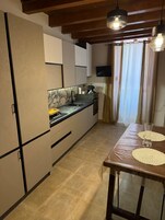 Cozinha com pia, fogão e armários, uma mesa de jantar com jogos americanos e uma TV fixada na parede.