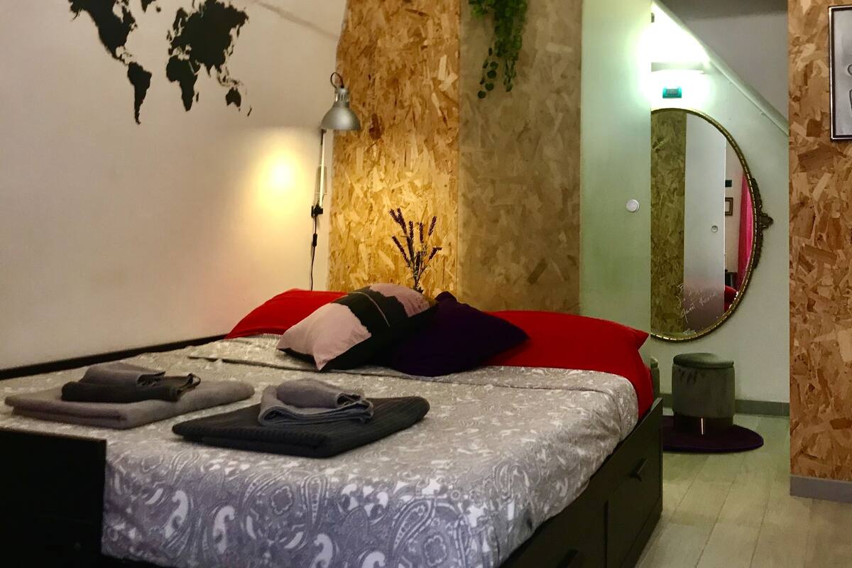 Um quarto moderno com cama, cabeceira vermelha, mapa-múndi na parede, lustre e espelho.