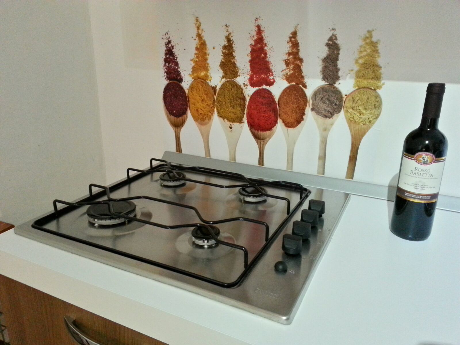 A kitchen with a gas stove and a bottle of Rosso Barletta wine.