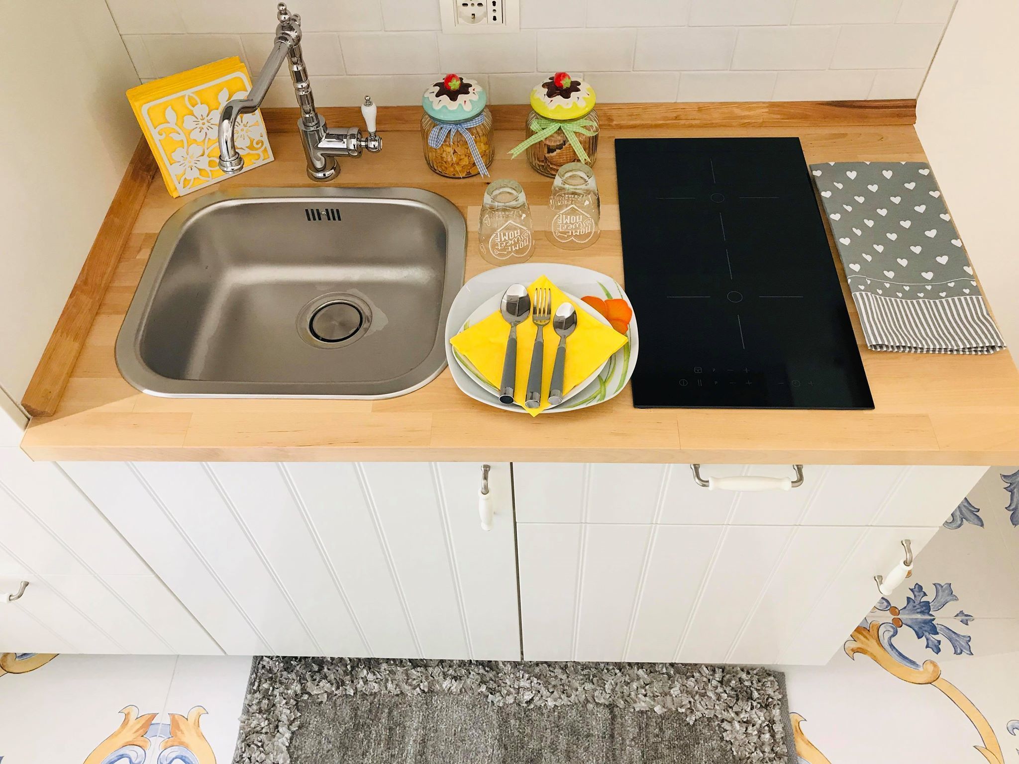 Una cocina con un lavamanos de acero inoxidable, una placa de inducción negra y una encimera de madera.
