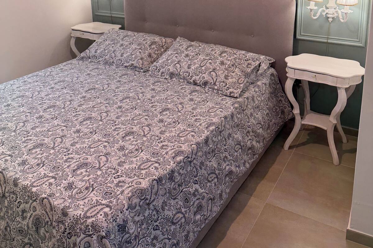 Quarto com cama, mesas de cabeceira e luminárias fixadas na parede.