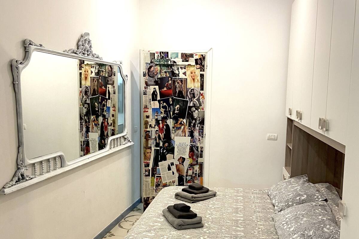 Quarto com cama, espelho, painel decorativo na parede e mesa de cabeceira.