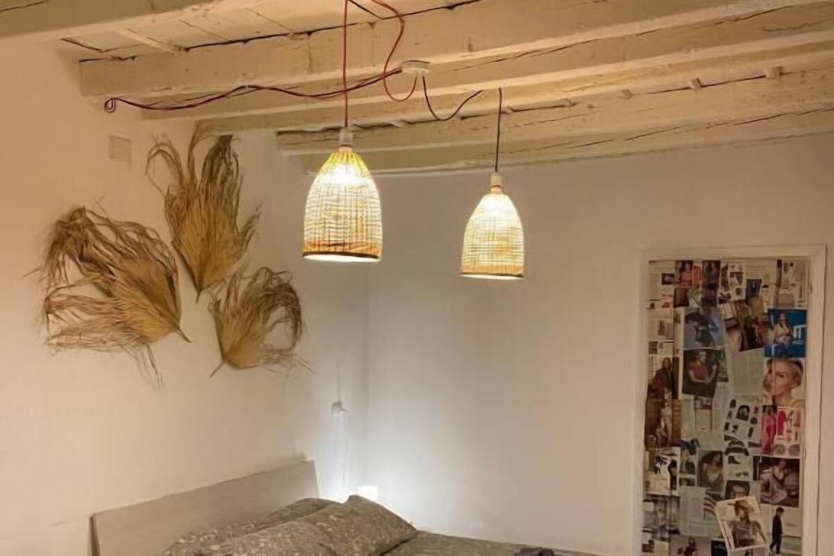 Quarto com cama, duas luminárias pendentes, mesa de cabeceira e parede com fotografias.