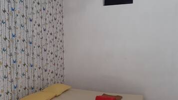 A room with a bed, a small window, and a patterned curtain.
