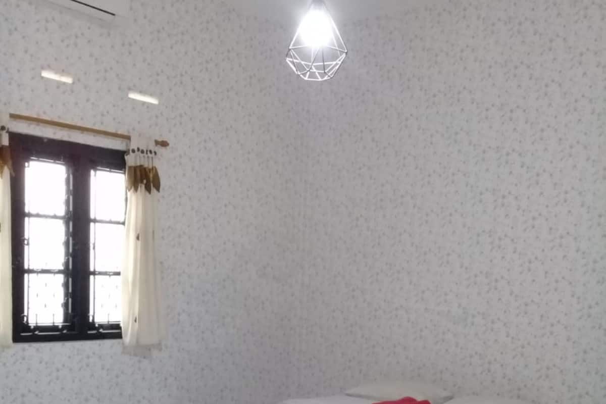 A bedroom with a bed, white curtains, a window, and a hanging light fixture.