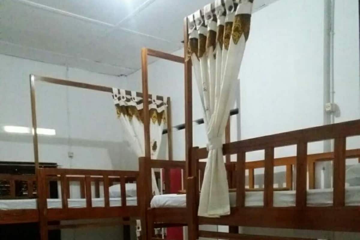 A dormitory room with bunk beds, wooden railings, and curtains.