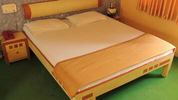 Un lit simple avec un cadre en bois et un matelas beige. Il y a une table de chevet avec un téléphone rouge et une lampe à côté du lit. La pièce est dotée d’une moquette verte et d’un papier peint à motifs.