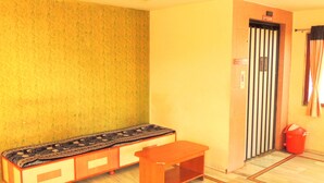 A room with a patterned wall, a bench, a small table, a radiator, and a door with a sign indicating the 2nd floor. - Hotel Greenpark (Danta)