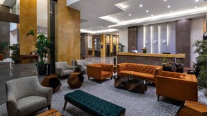 Een moderne lobby met een receptiebalie, een zithoek en potplanten.