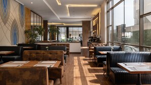 Een modern restaurant met lederen zitjes en tafels, grote ramen en een bar in het midden.
