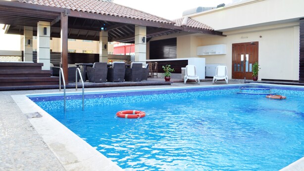 Piscina com borda em azulejo, cadeiras de descanso e área de estar coberta.