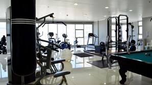 Uma academia com equipamentos de exercício, mesa de bilhar e amplas janelas.