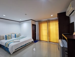 A hotel room with a large bed, a flat-screen TV, a desk, and a window with yellow curtains.